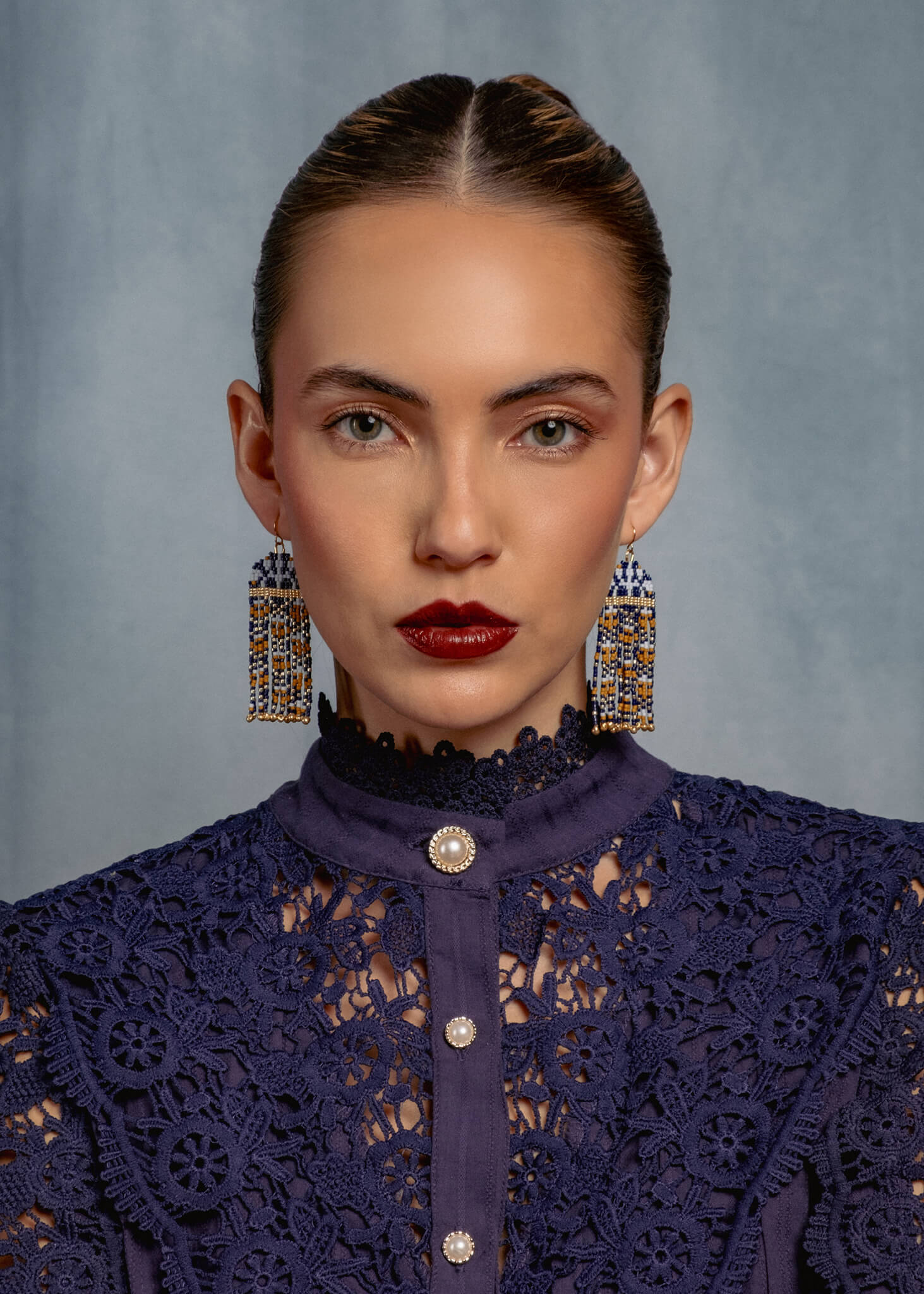 Woman wearing a dark blue lace top with large earrings against a gray background