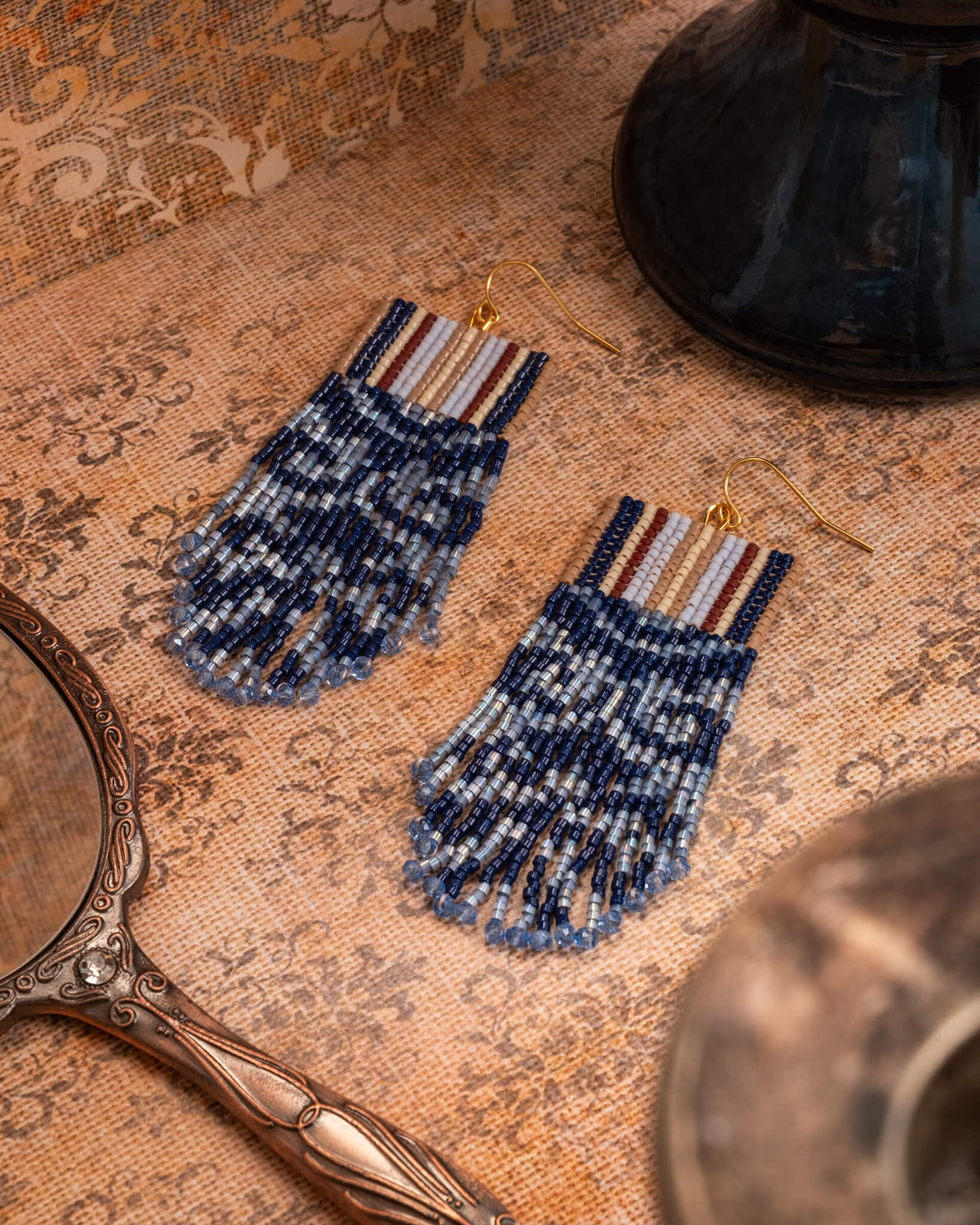 Pair of beaded earrings on a textured surface with vintage decor elements.