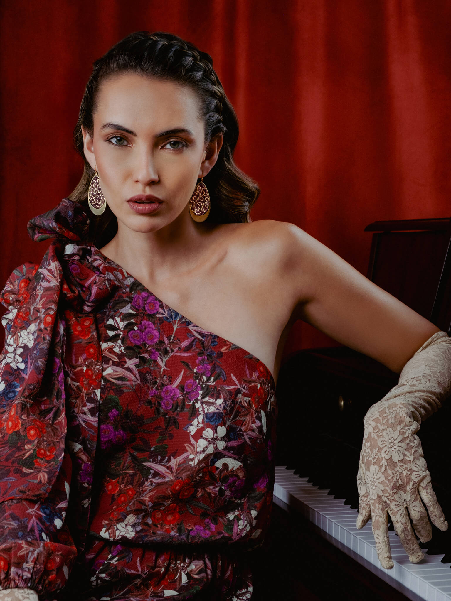 Woman in a floral dress and gloves sitting at a piano with a red curtain background