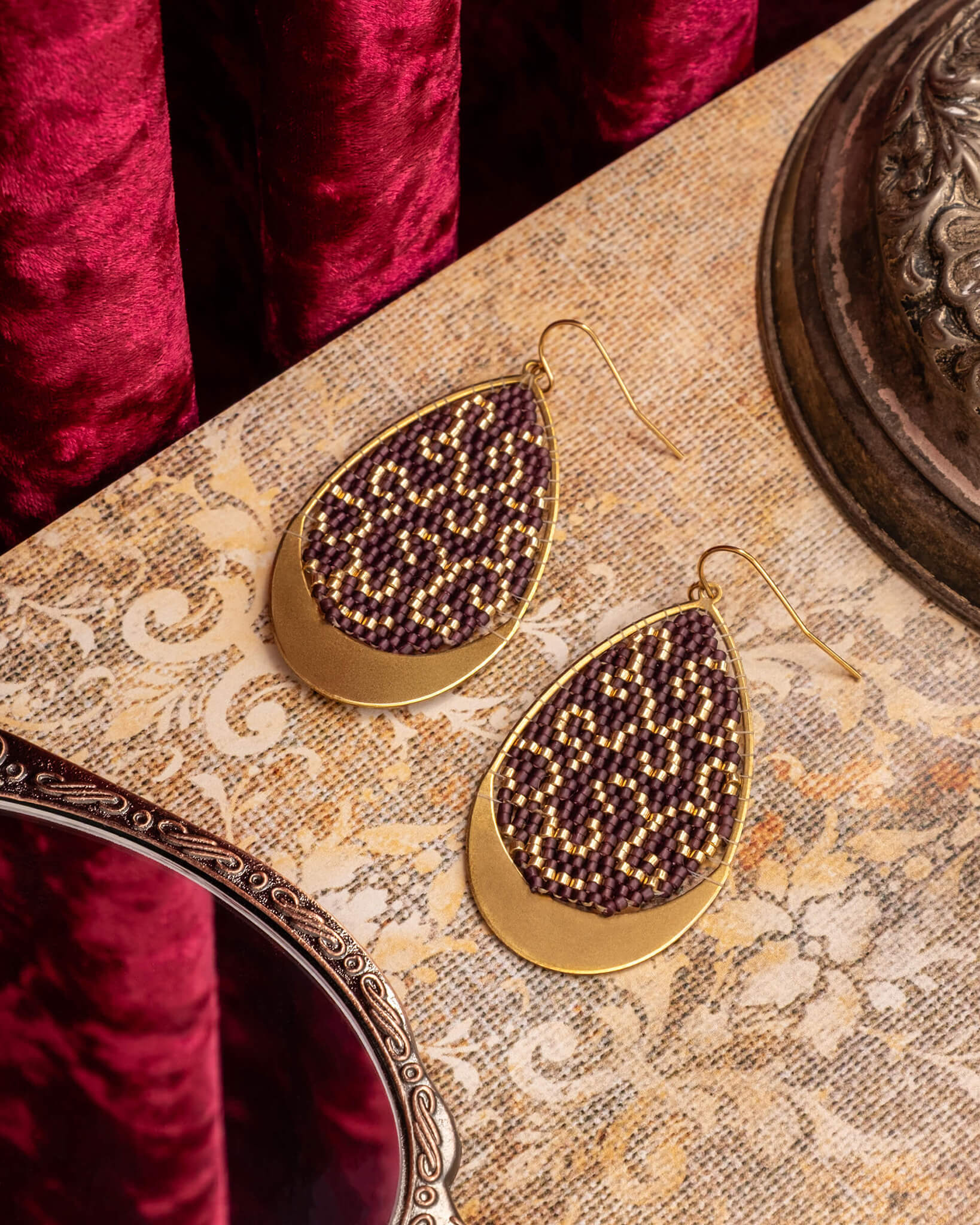 Gold earrings with purple beads on a decorative surface
