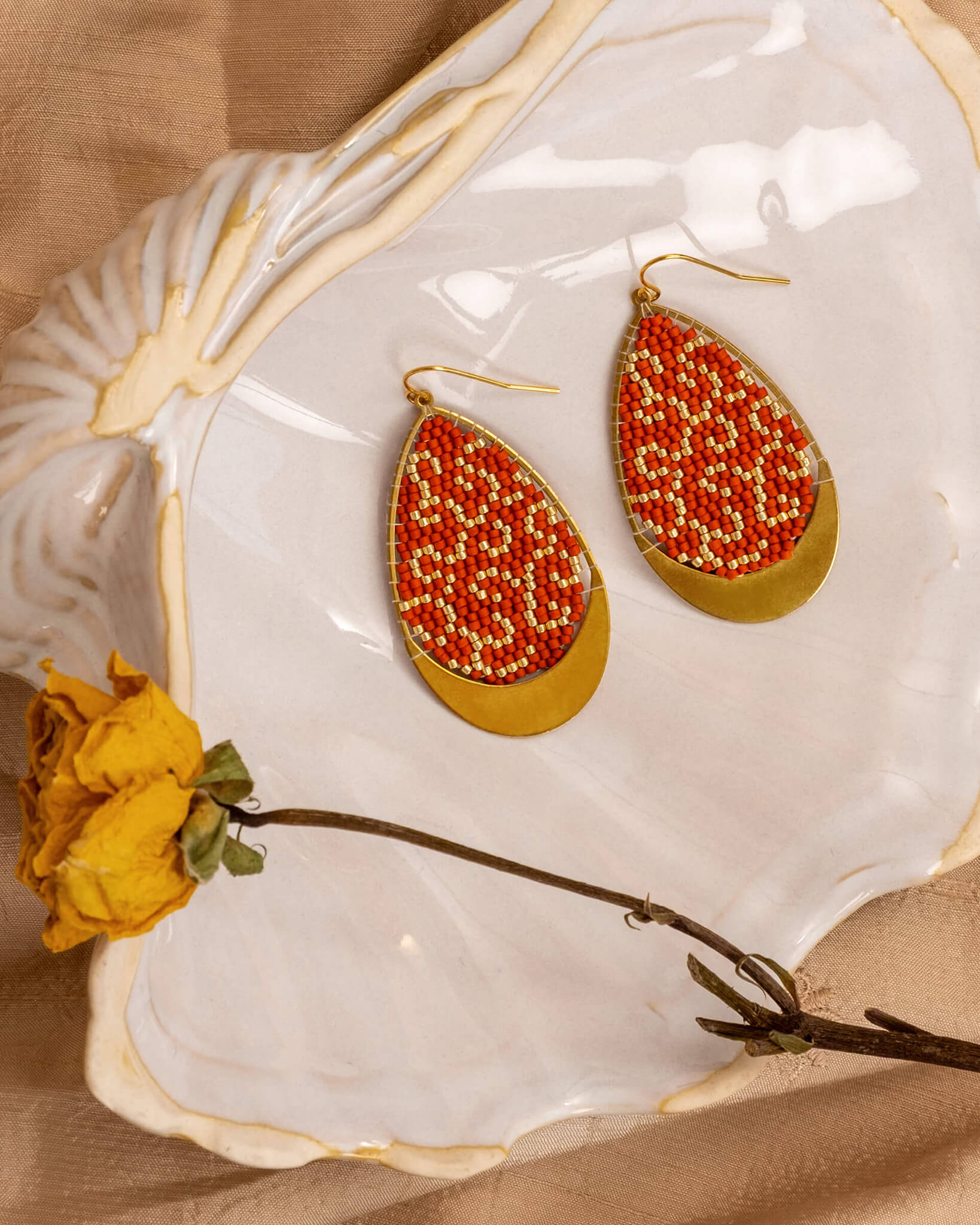 Teardrop-shaped earrings with red and gold beads on a white shell with a yellow flower.