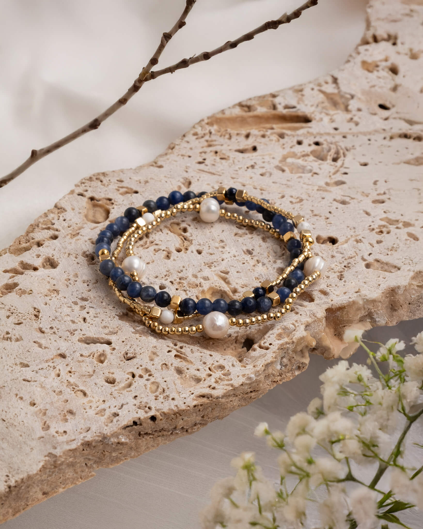 Beaded bracelet with blue and gold accents on a stone surface with flowers.
