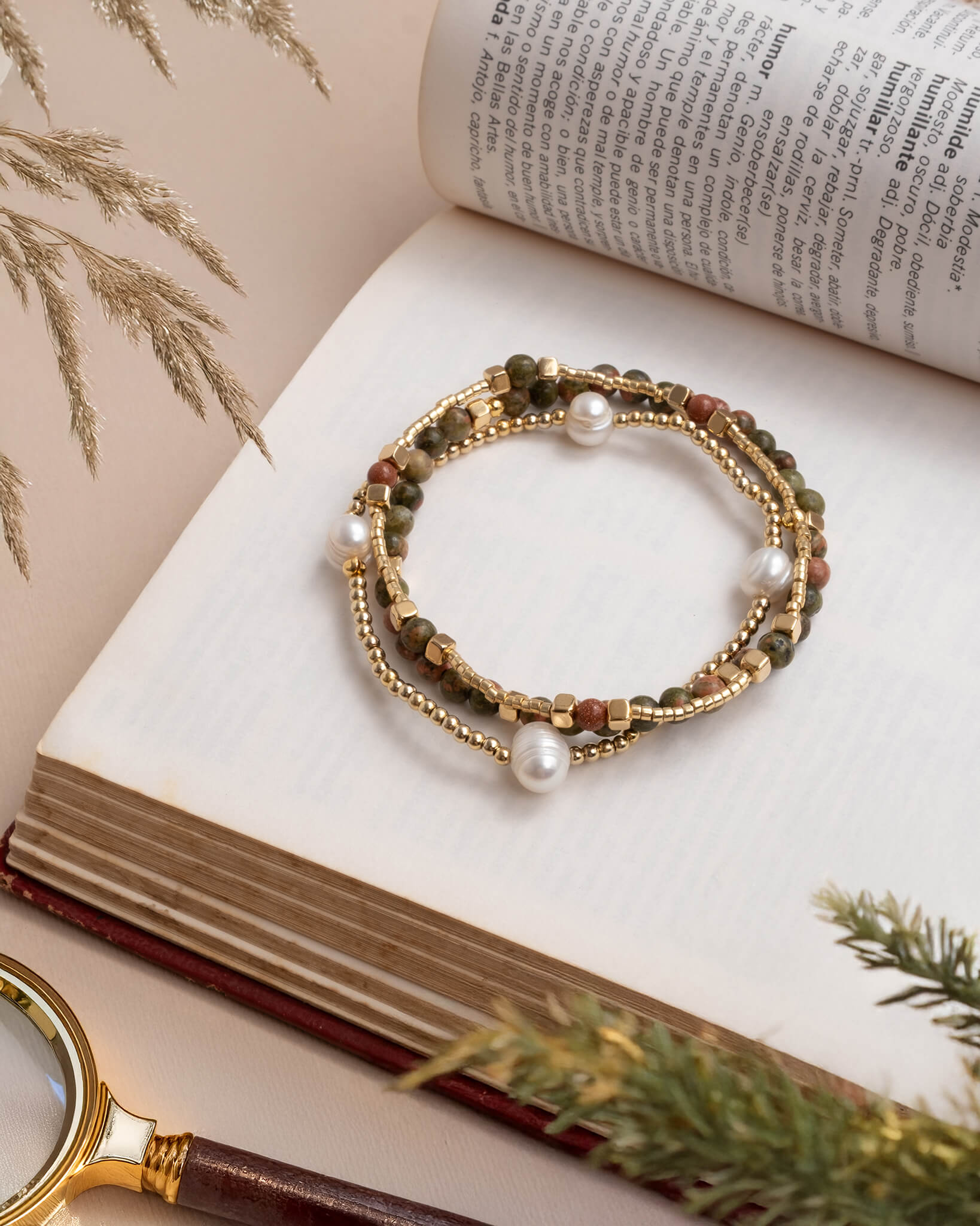 Bracelet with pearls and stones on an open book with a magnifying glass and decorative elements.